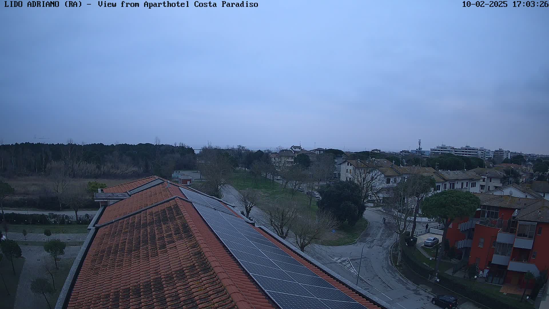 A rooftop with solar panels overlooks a residential area under a cloudy, dusky sky.