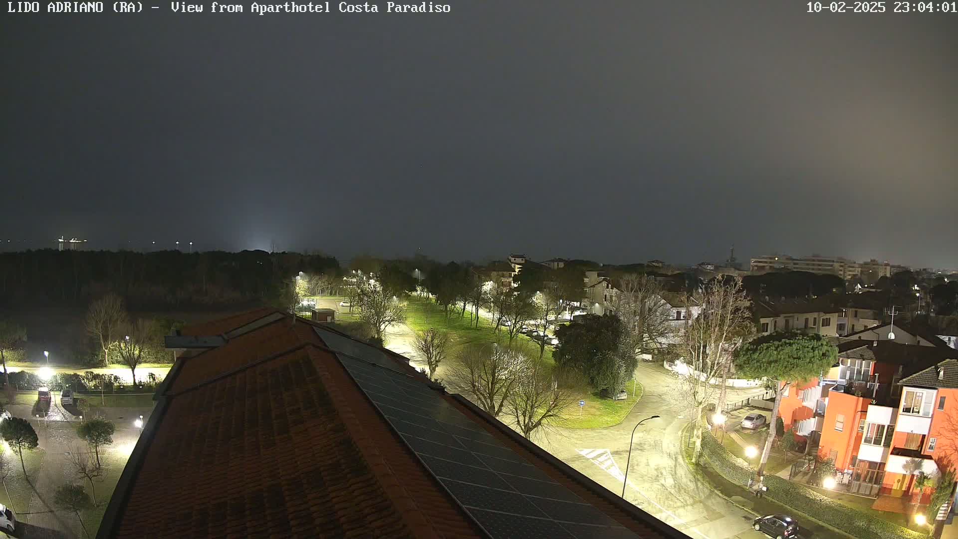 A nighttime view of a residential area with streetlights illuminating roads and buildings under a dark, foggy sky.