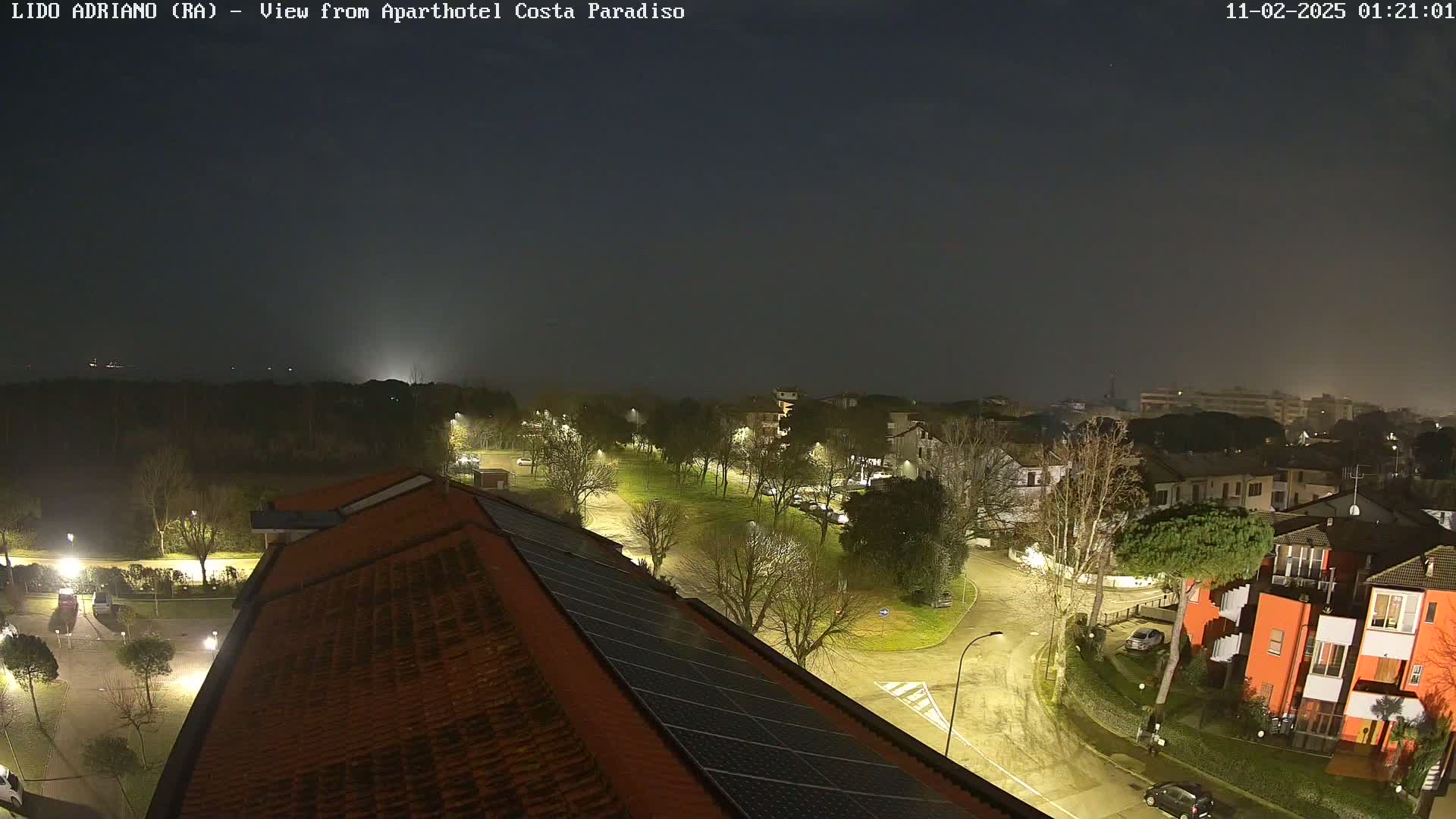 A nighttime view of a residential area with streetlights illuminating roads and buildings under a hazy sky.