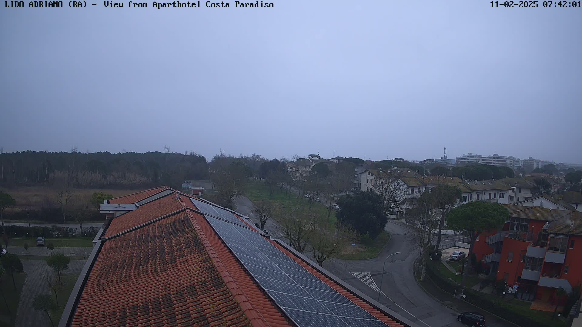 An overcast sky overlooks a residential area with a red-tiled roof featuring solar panels in the foreground.