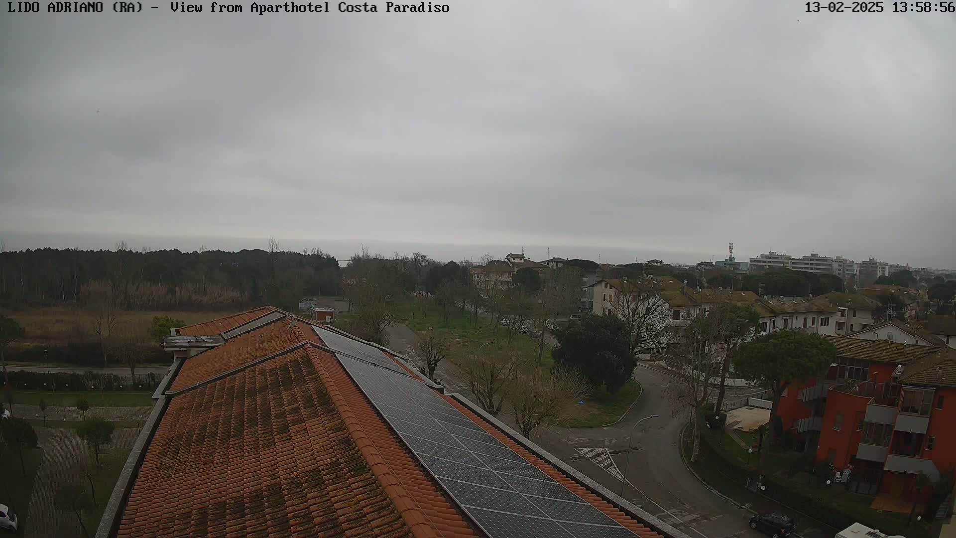 A view from a rooftop with solar panels shows a residential area with overcast skies and a distant body of water.