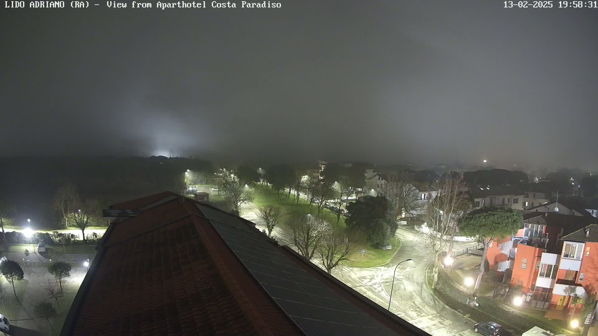 A nighttime view of a town covered in fog, showing snow-dusted roads and buildings illuminated by streetlights.