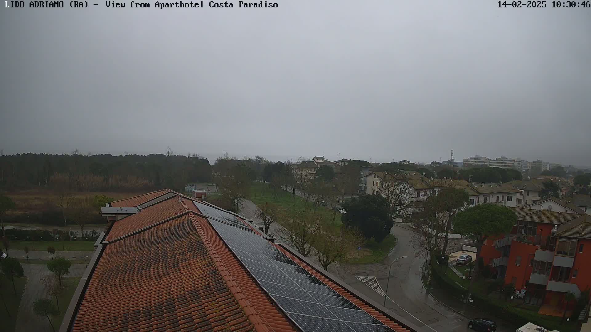 A view from a rooftop with solar panels shows a residential area on an overcast day.