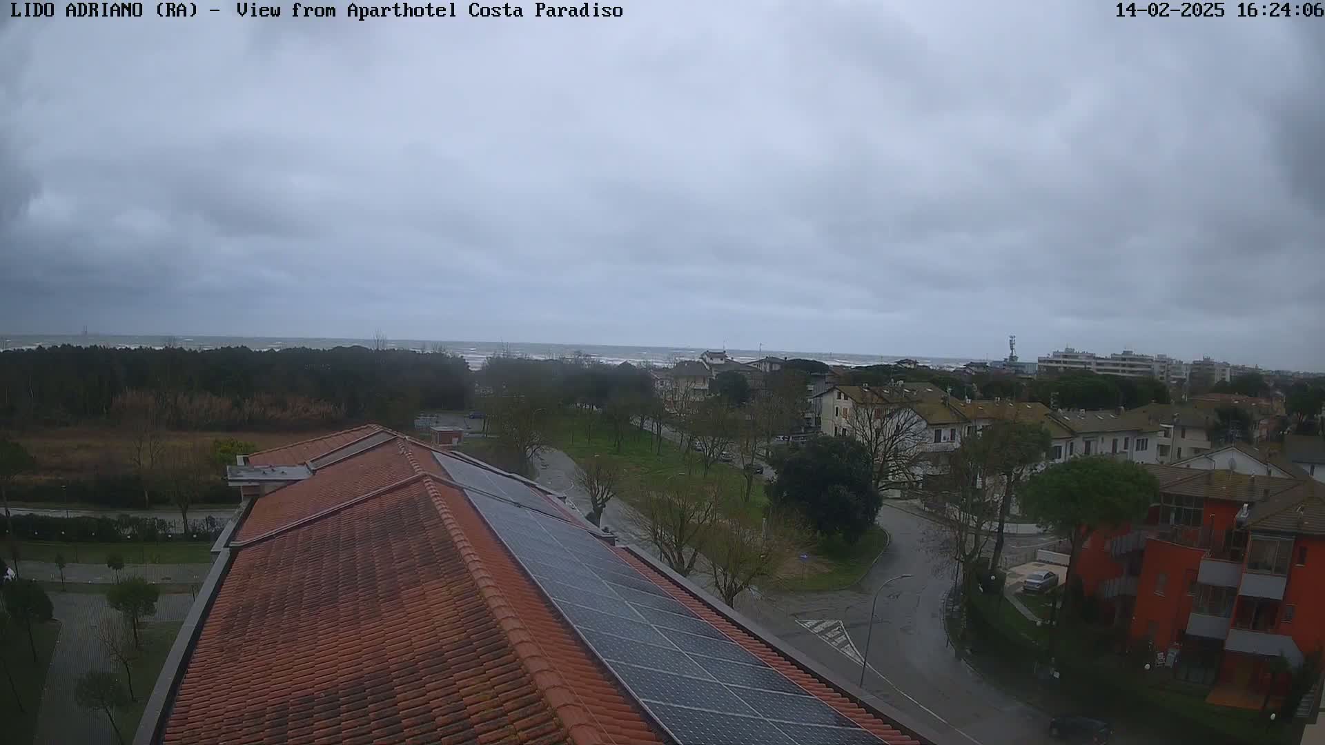A view from a rooftop with solar panels shows a cloudy day overlooking a coastal town and a choppy sea.