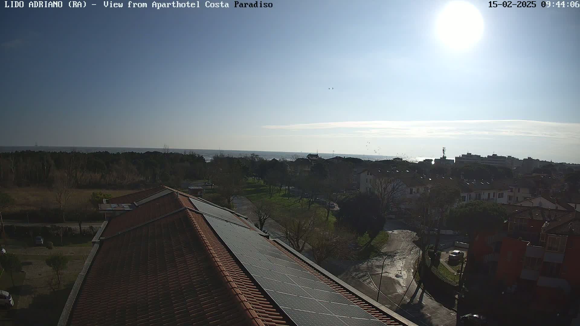 A sunny view from a rooftop with solar panels shows a residential area next to a calm ocean.