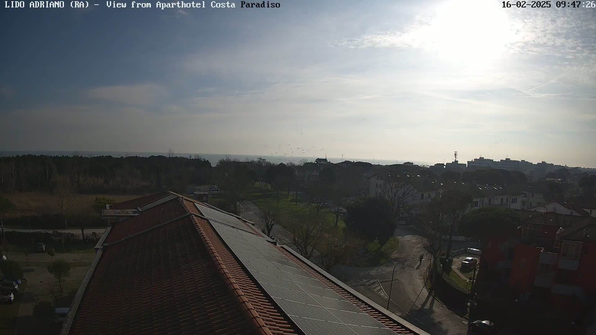 A rooftop view on a sunny day shows a residential area with a calm sea in the background.