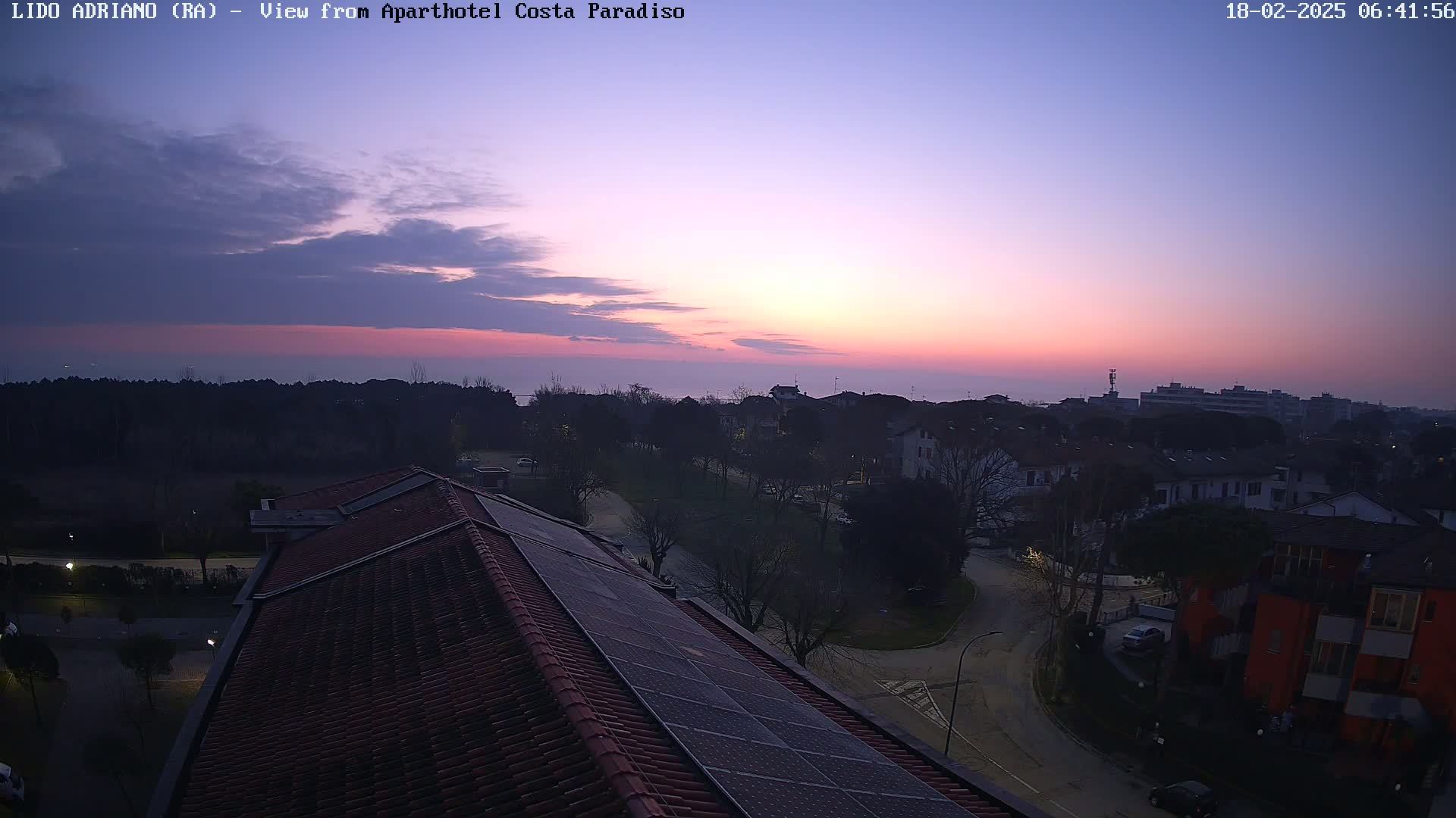 A sunrise over a residential area with a view from a rooftop featuring solar panels, under a mostly clear sky.