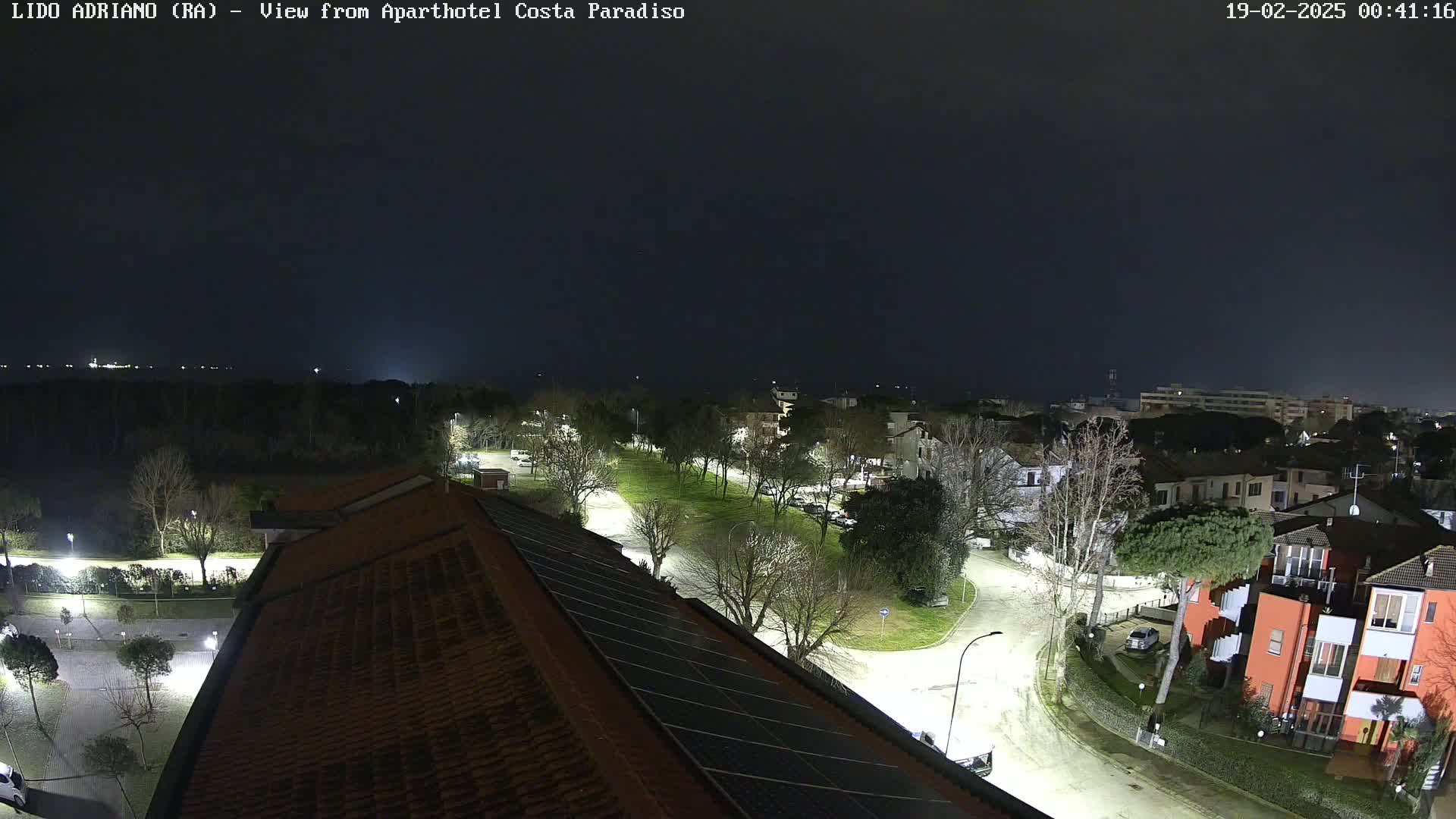 A nighttime view of a residential area near a body of water, illuminated by streetlights under a dark, overcast sky.