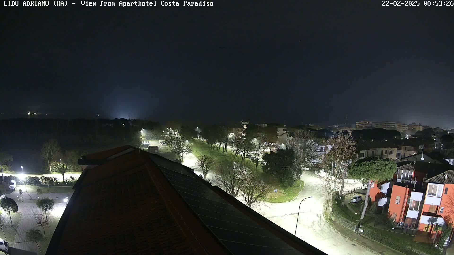 A nighttime aerial view of a residential area with streetlights illuminating roads and trees under a dark, cloudy sky.