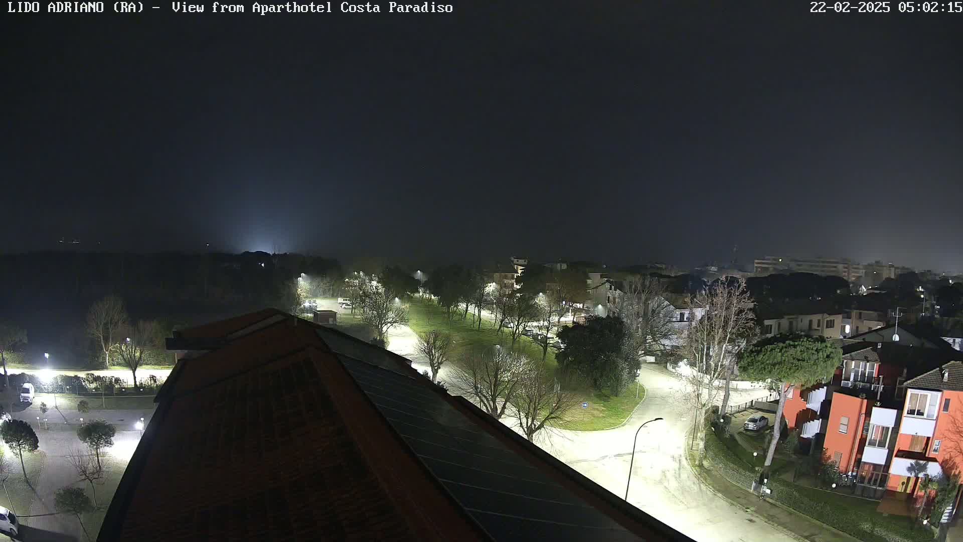 A nighttime view of a residential area with a park, illuminated by streetlights under a foggy sky.