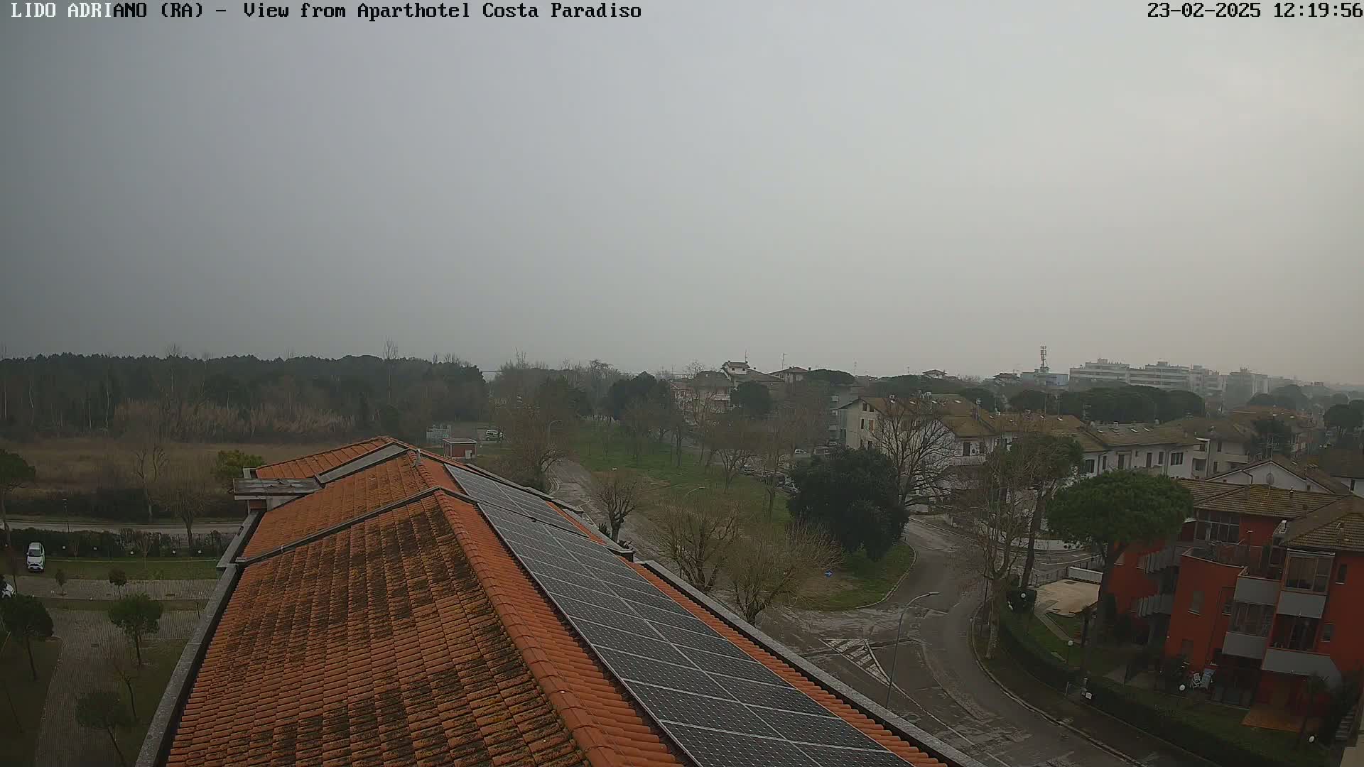 A view of a residential area on an overcast day, seen from a building rooftop with solar panels.