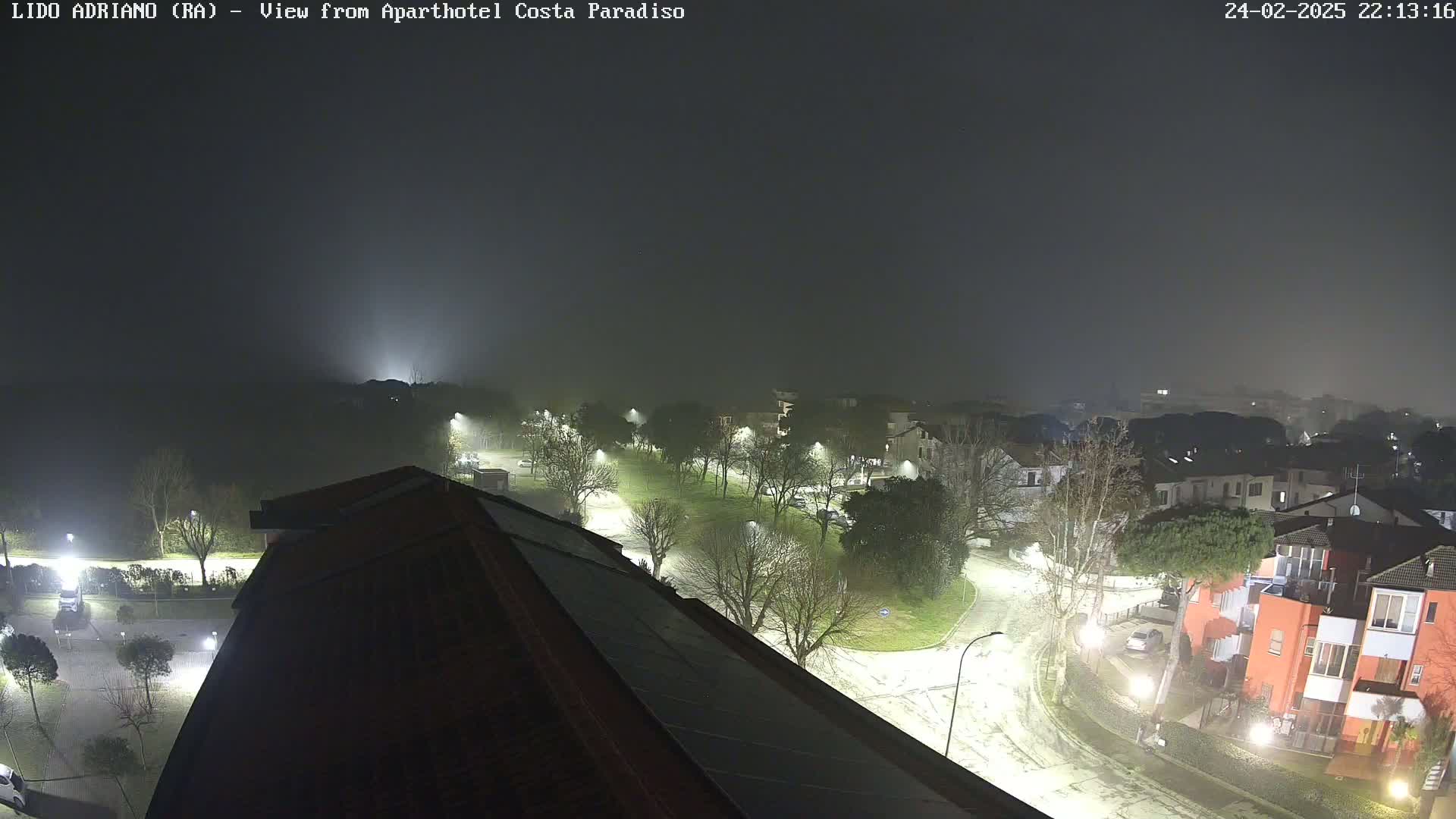 A nighttime view of a foggy residential area with streetlights illuminating roads and buildings.
