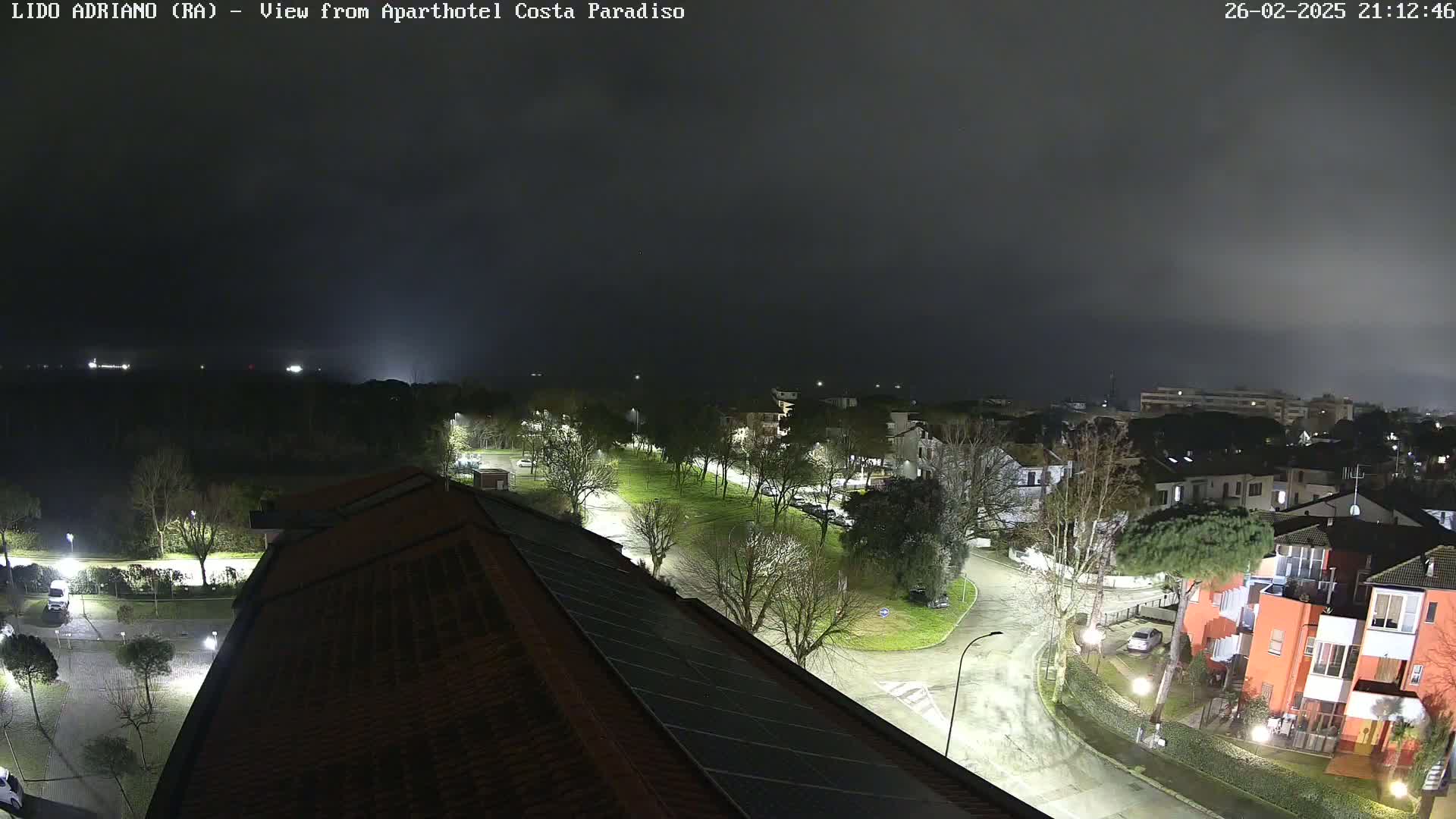 A nighttime, overcast view of a residential area with streetlights illuminating roads, buildings, and trees.