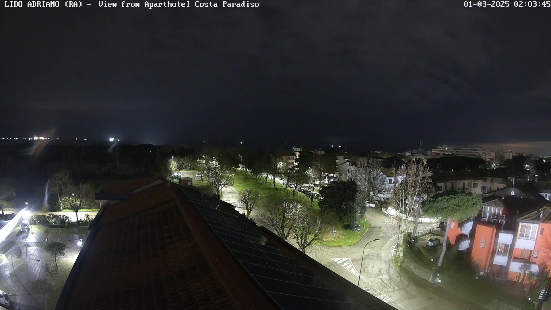 A nighttime view of a residential area with wet streets, under a dark, cloudy sky.