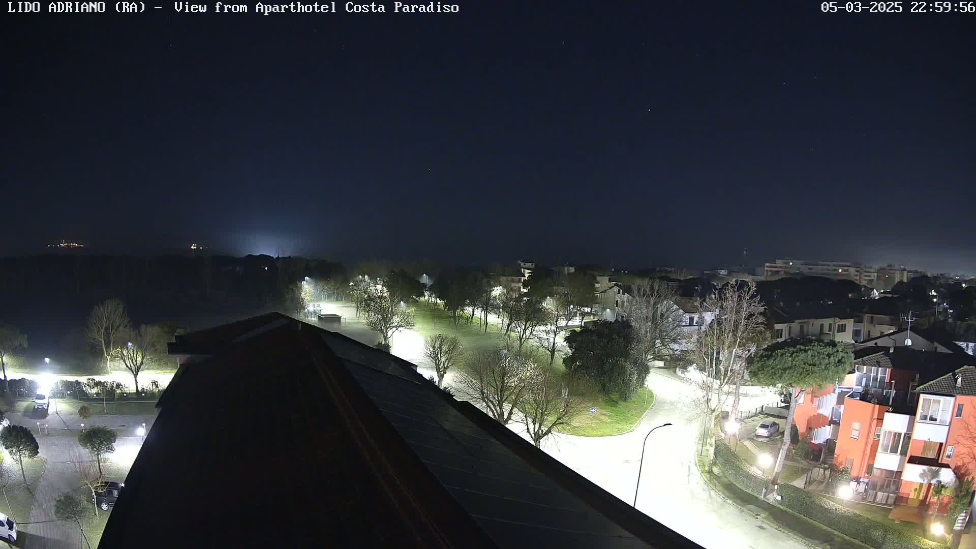 A nighttime aerial view of a residential area with a park and roadway, illuminated by streetlights under a clear, dark sky.