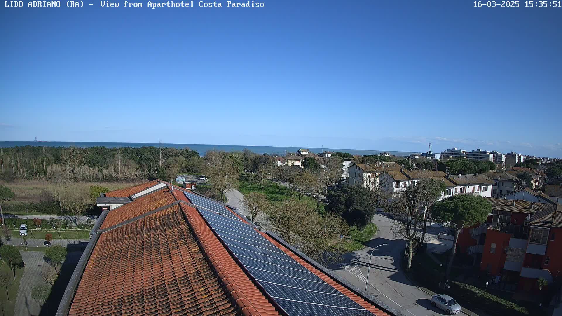 A clear blue sky overlooks a coastal town with a sea view, a tiled roof with solar panels in the foreground.
