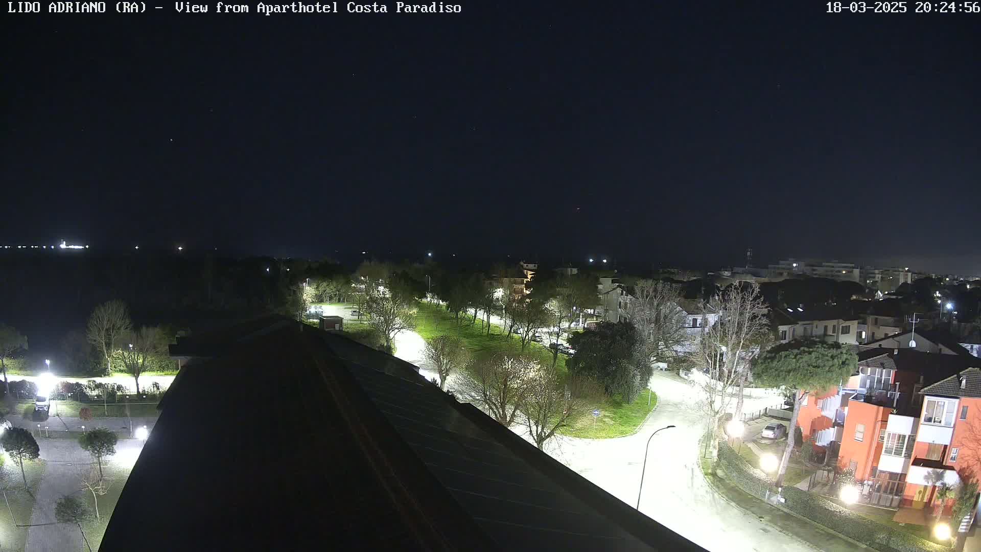 A nighttime view of a residential area near a body of water, illuminated by streetlights, under a clear, dark sky.