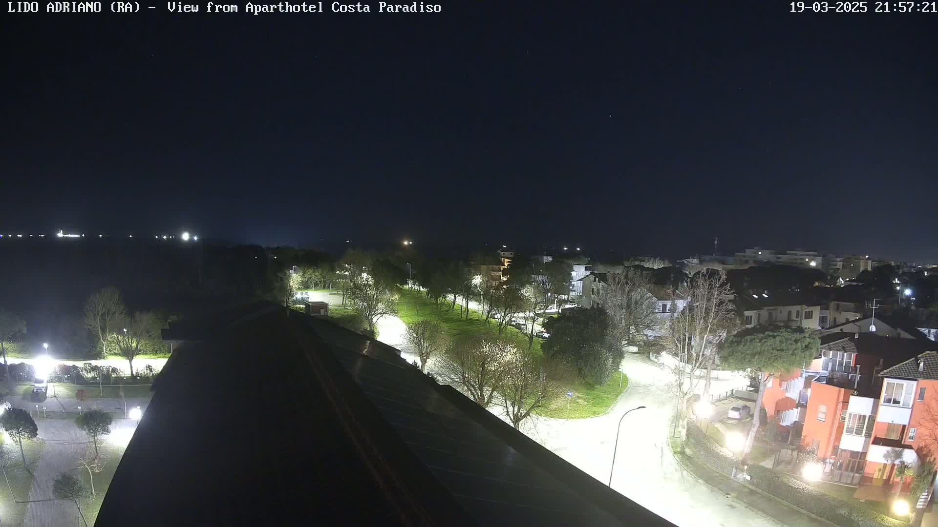 A nighttime aerial view of a residential area with roads, trees, and buildings, under a clear sky.