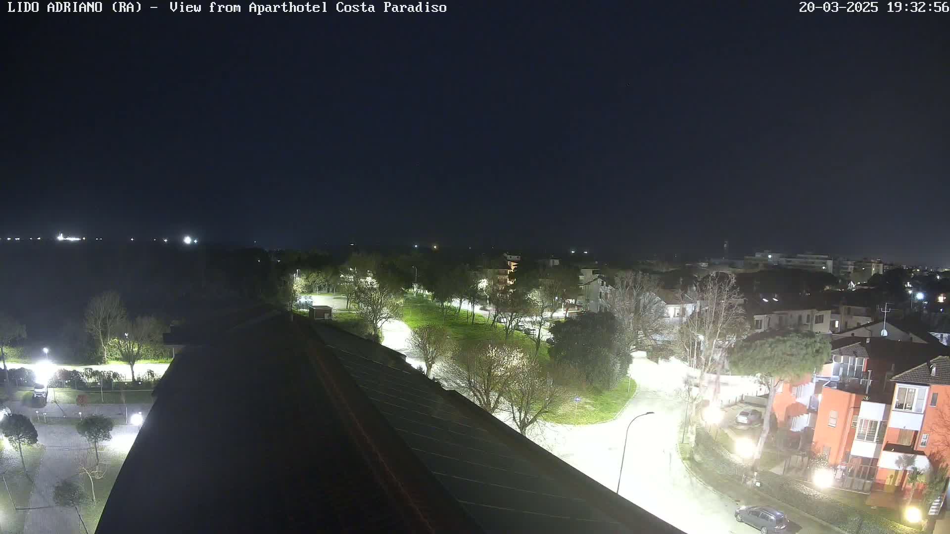 A nighttime view of a residential area with trees and roads illuminated by streetlights under a dark, clear sky.