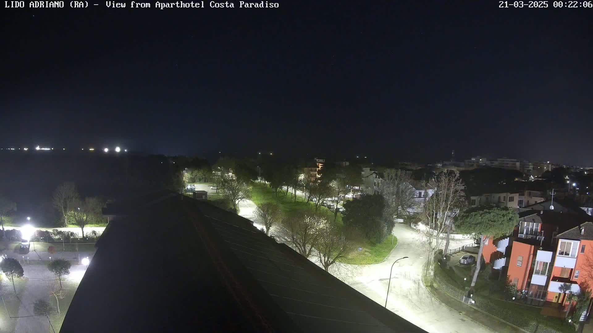 A nighttime, overhead view of a residential area with roadways, trees, and buildings illuminated by streetlights under a clear, dark sky.