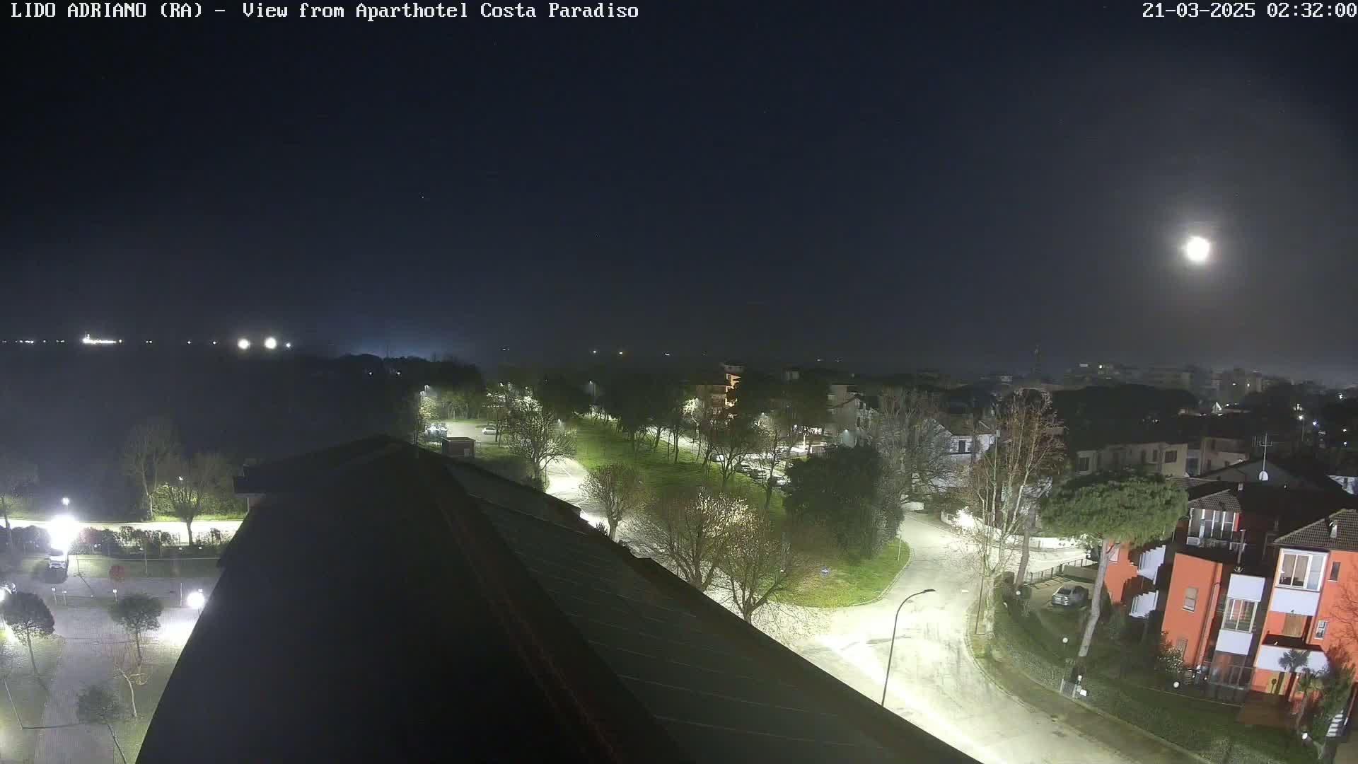A nighttime view of a residential area with a bright moon, illuminated streets, and trees.