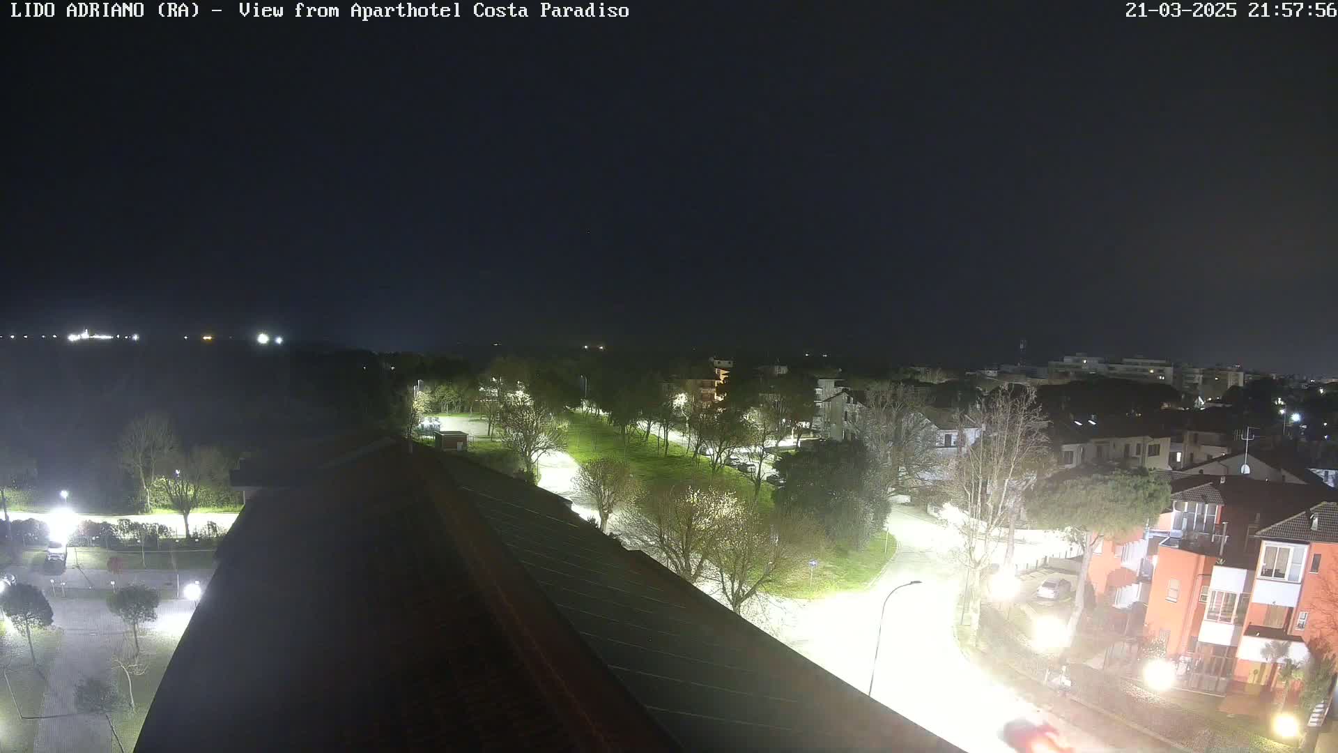 A nighttime view of a residential area with brightly lit streets and trees, under a clear, dark sky.
