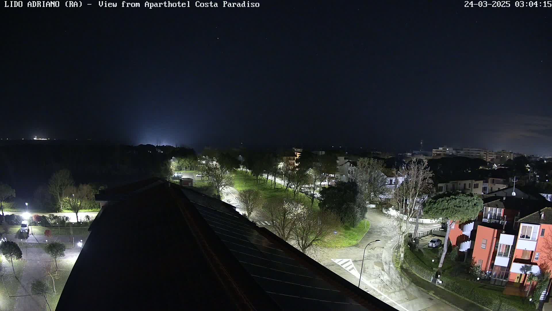 A nighttime, high-angle view of a residential area with streetlights illuminating roads, trees, and buildings under a dark, clear sky.