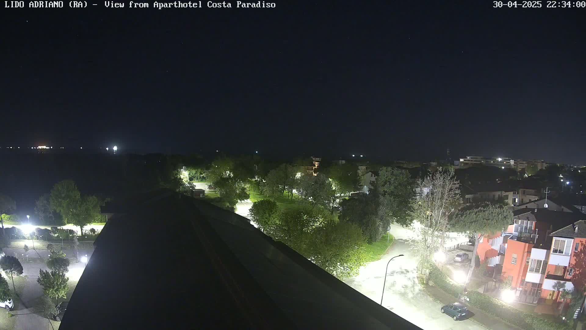 A nighttime aerial view shows a residential area with streetlights illuminating roads, buildings, and trees under a clear, starlit sky.