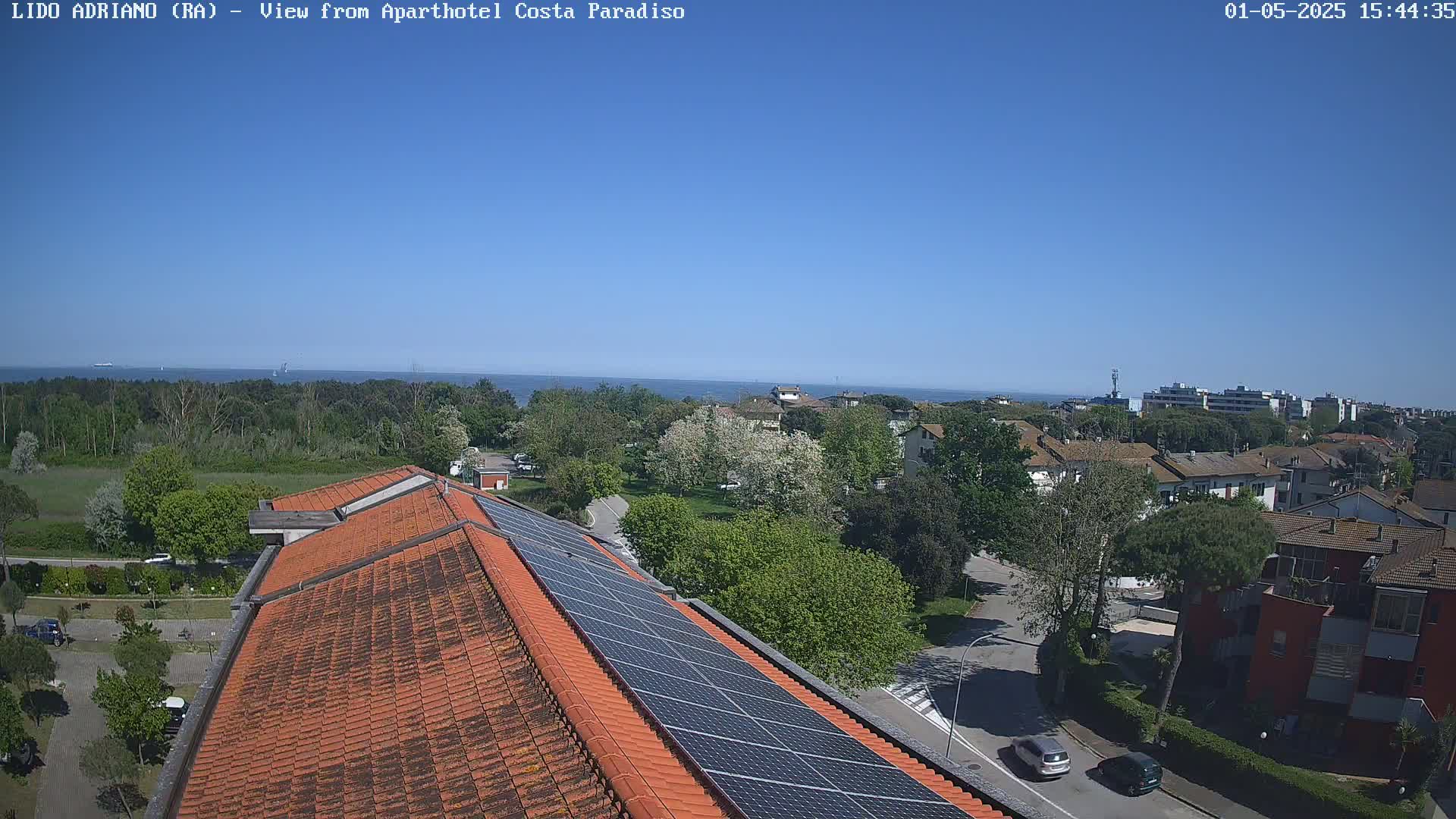 A rooftop with solar panels overlooks a residential area and a calm ocean under a clear blue sky.