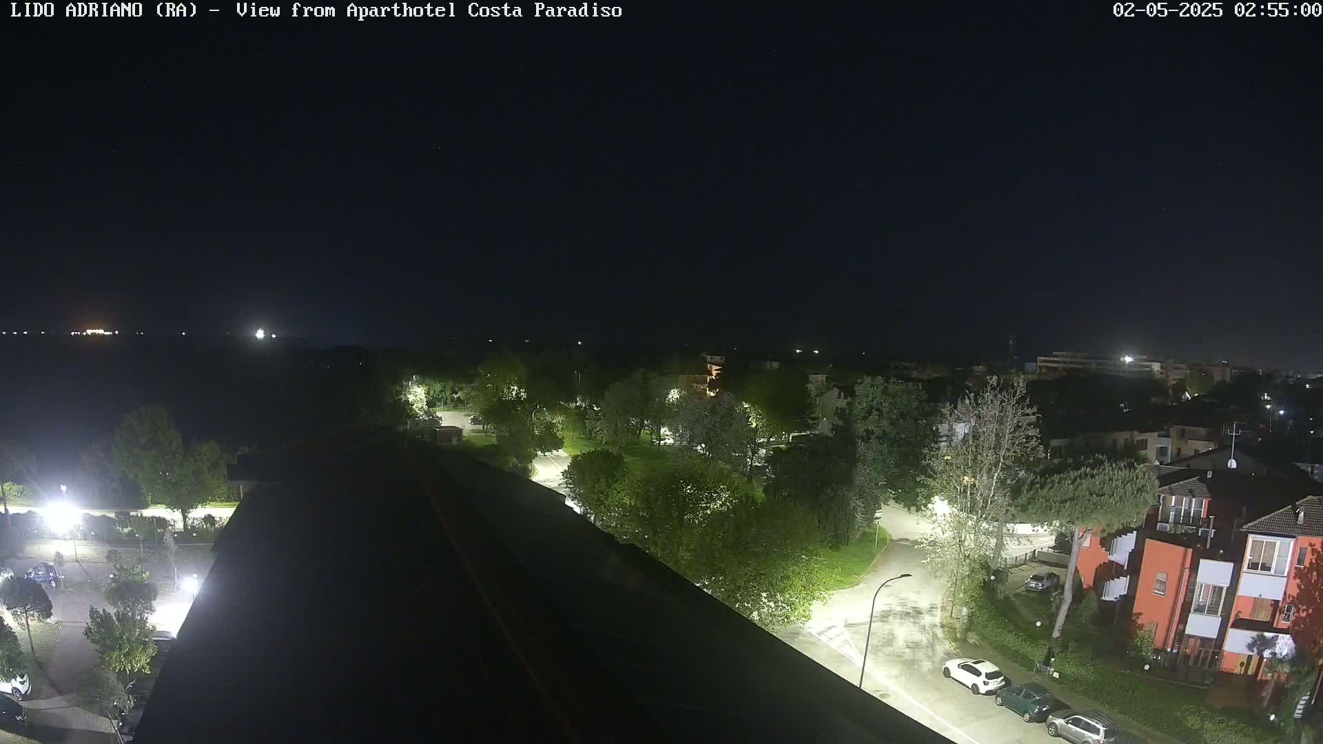 A nighttime view of a residential area with streetlights illuminating trees, roads, and buildings under a clear, dark sky.