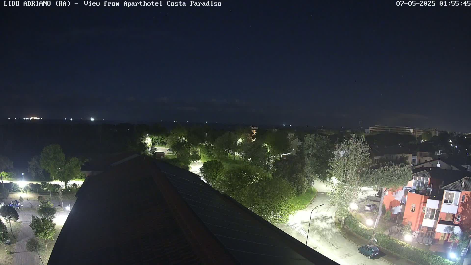 A nighttime aerial view of a residential area with tree-lined streets and buildings, under a clear, dark sky.