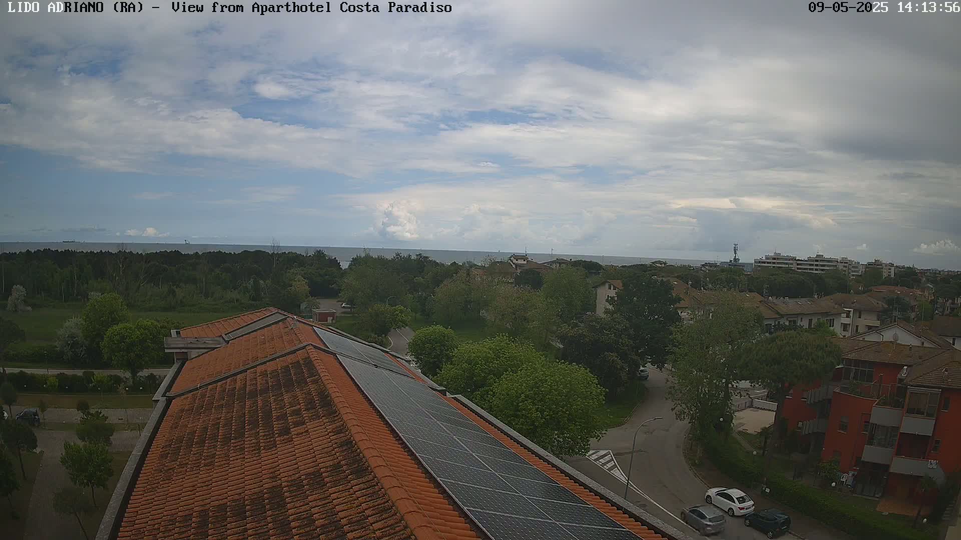A partly cloudy day overlooks a coastal town with a view of the sea from a rooftop with solar panels.