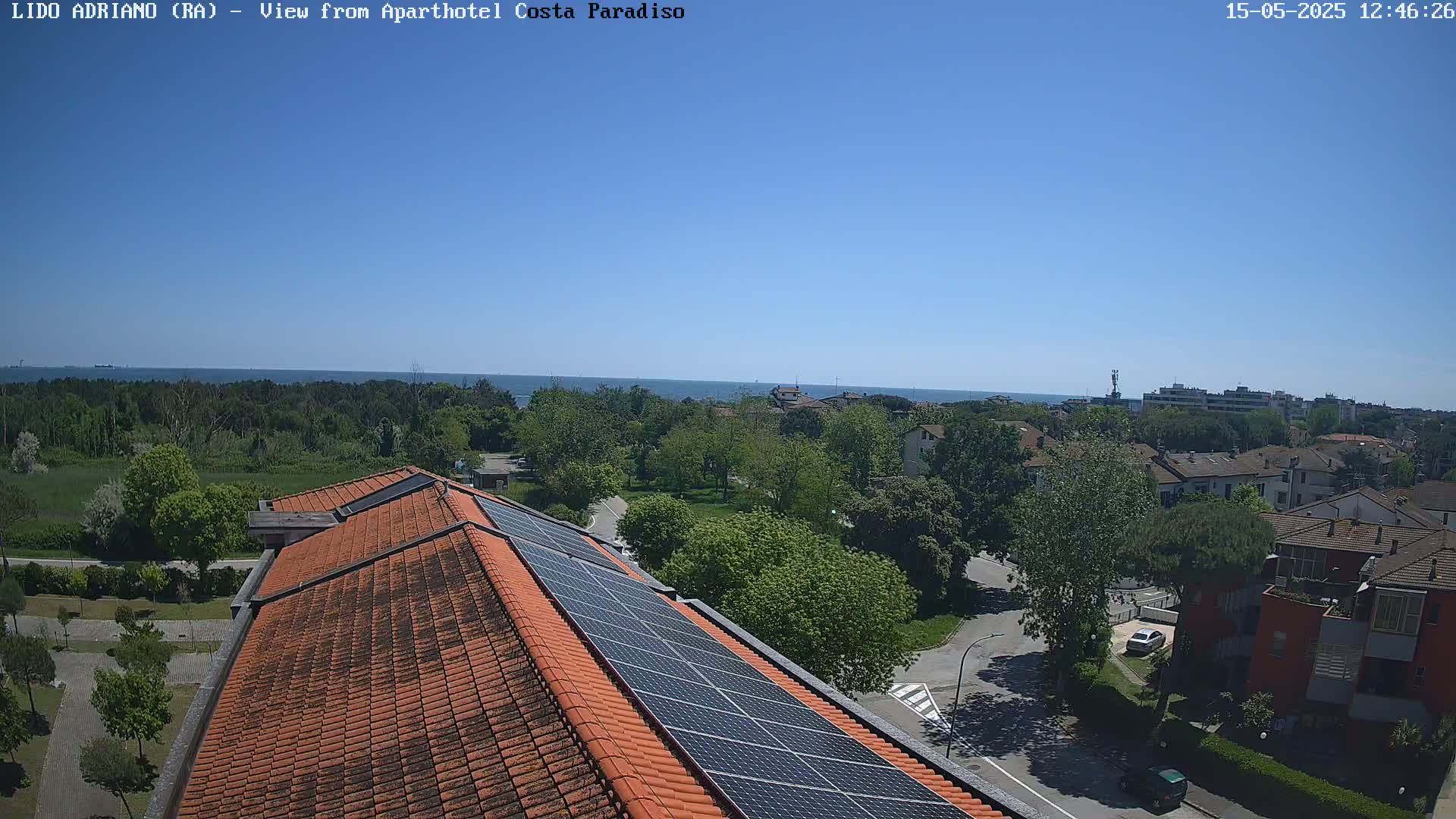 A clear, sunny day overlooks a coastal town with a view of the sea from a rooftop with solar panels.