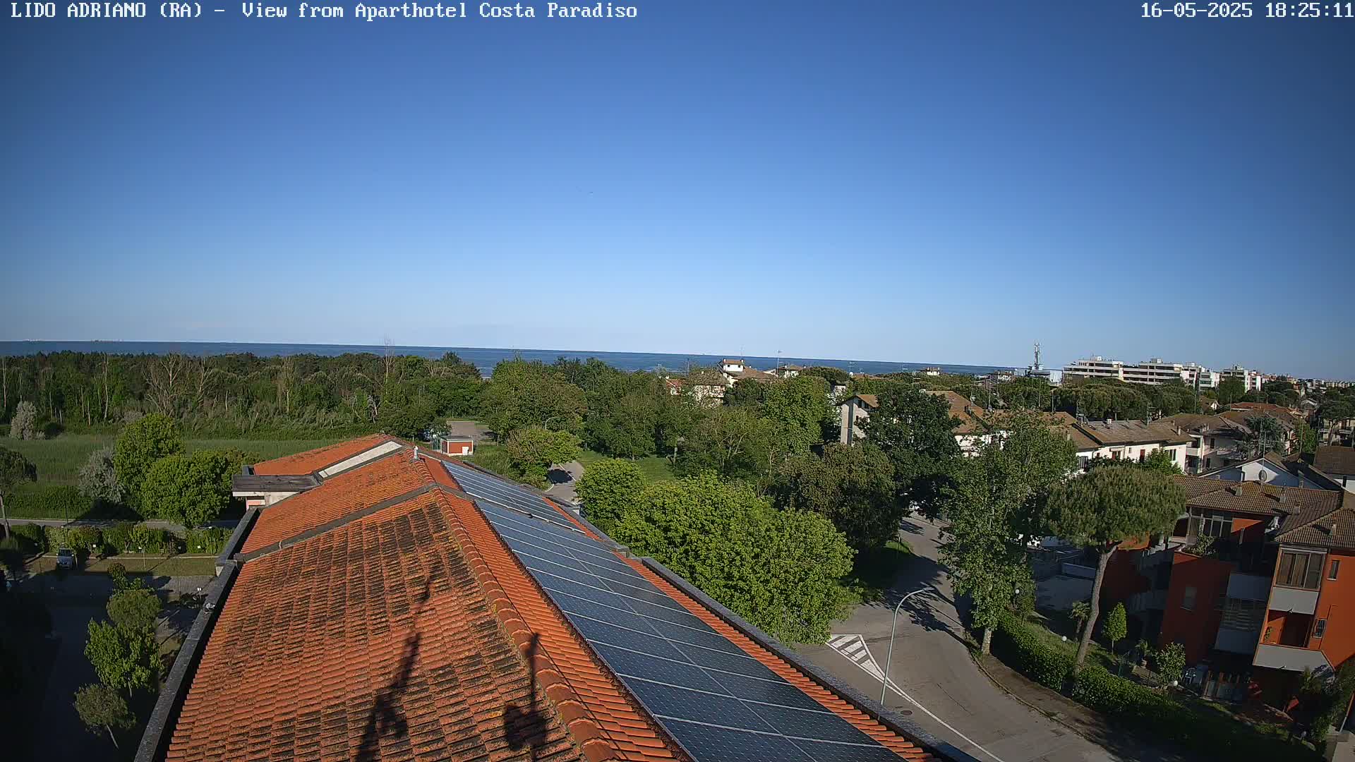 A rooftop with solar panels overlooks a seaside town on a clear, sunny day.
