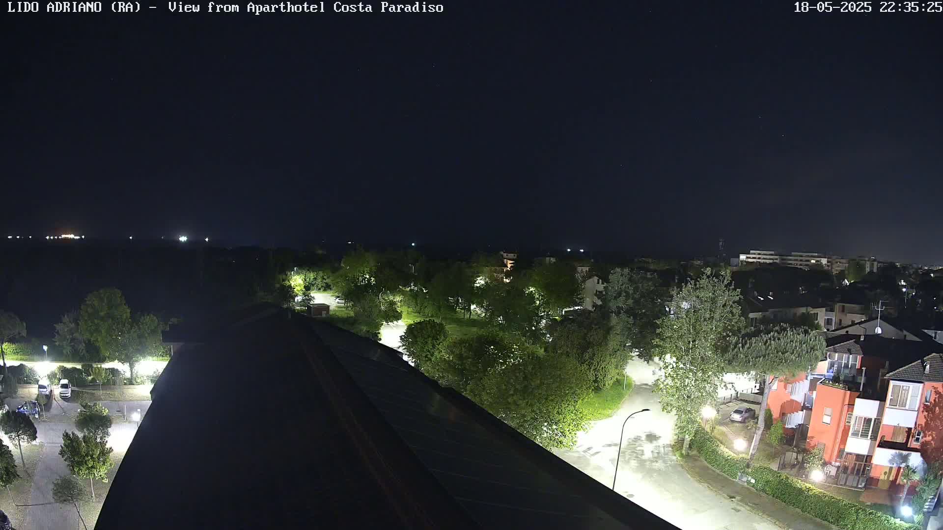 A nighttime, overhead view of a residential area with streetlights illuminating buildings, trees, and roads under a clear, dark sky.