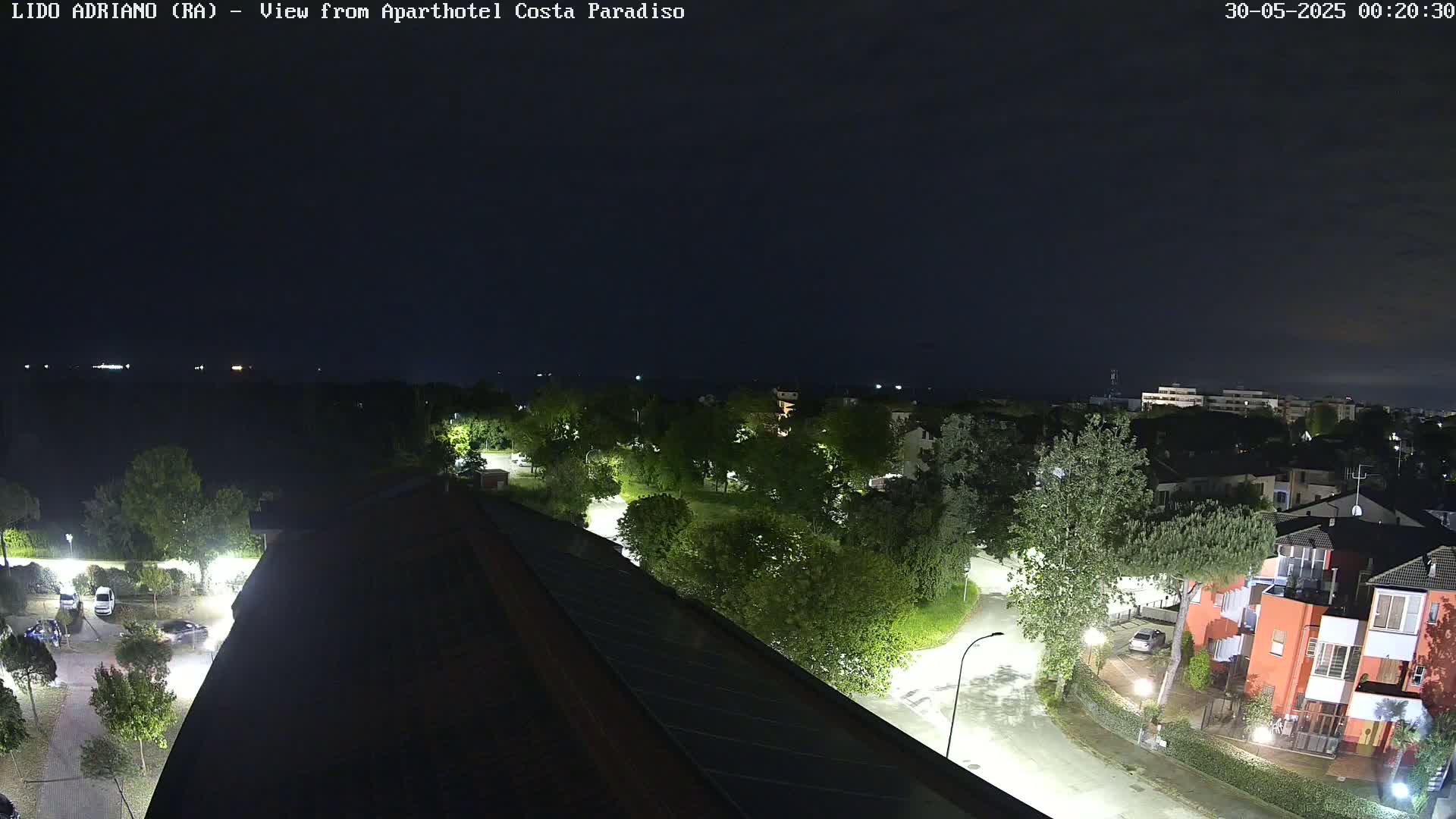 A nighttime aerial view shows a residential area with streetlights illuminating roads and trees, under a dark, clear sky.