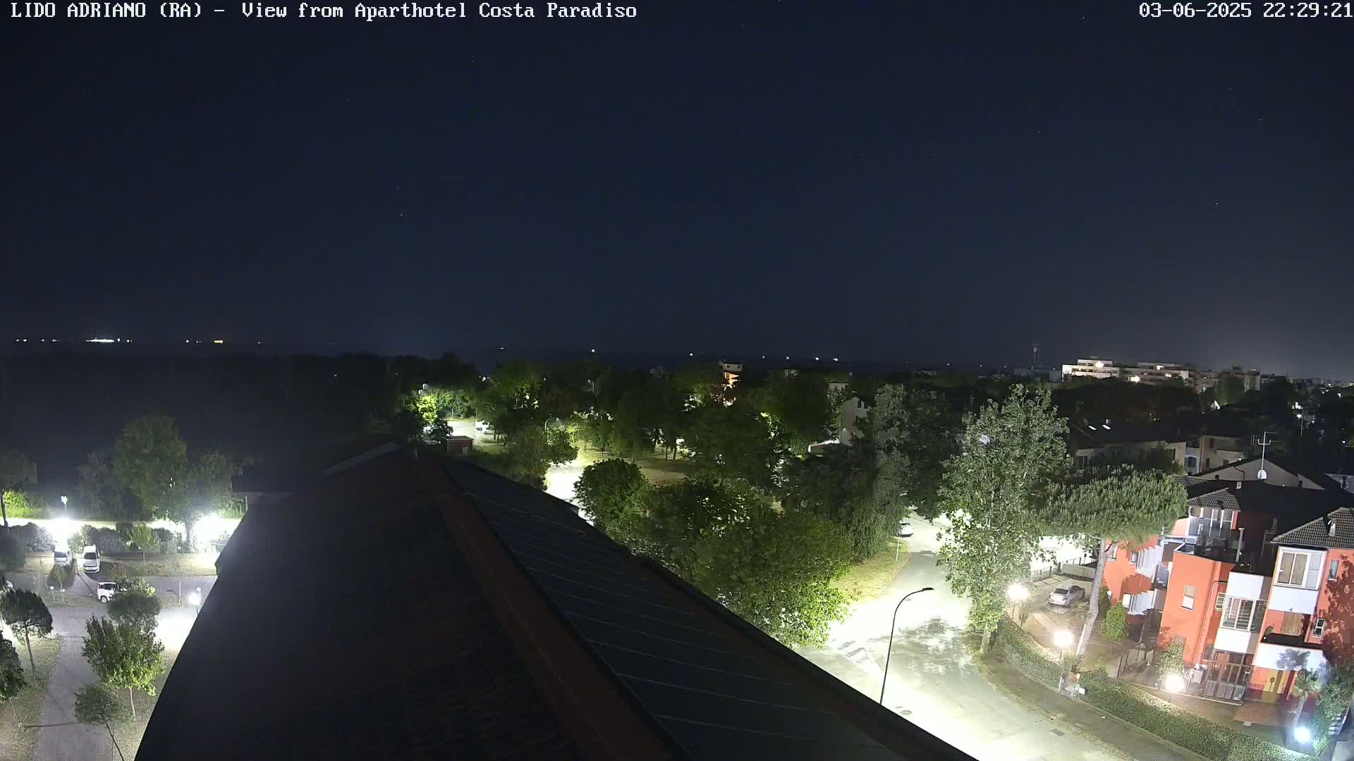 A nighttime view of a residential area with trees and buildings, lit by streetlights, under a clear, dark sky.