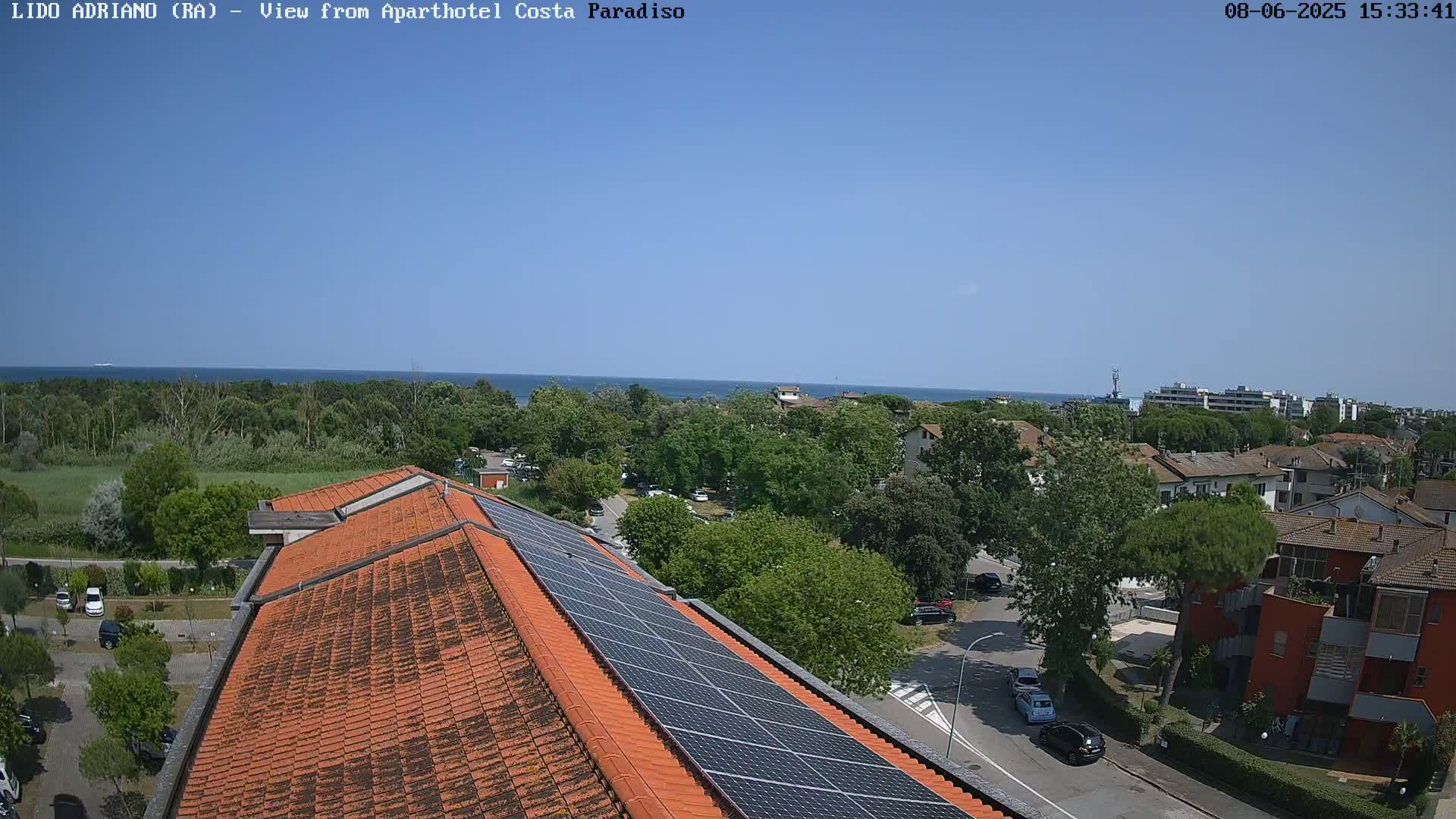 A rooftop view of a building with solar panels, overlooking a seaside town on a sunny day.