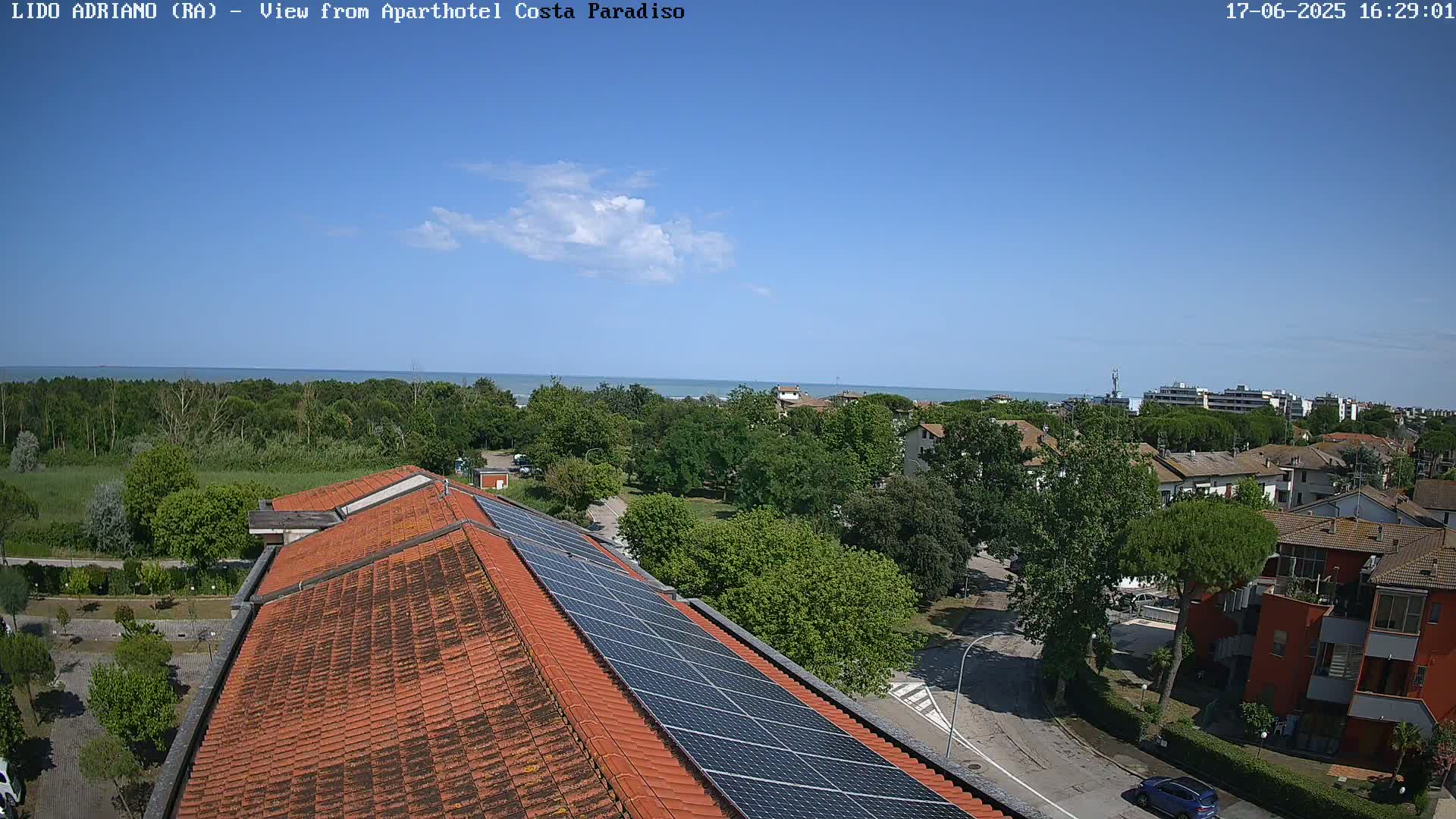 A rooftop with solar panels overlooks a coastal town under a mostly clear blue sky.
