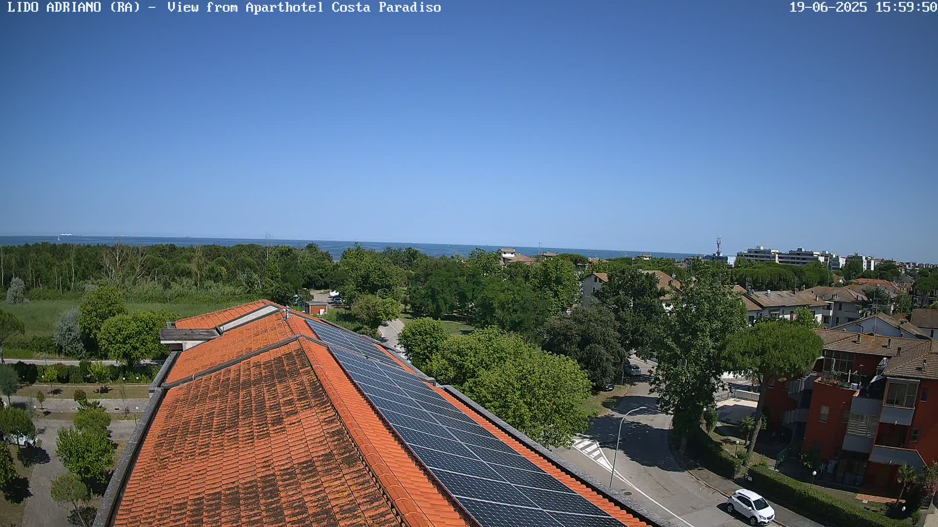 A clear, sunny day overlooking a coastal town with a building featuring solar panels on its roof, all situated near a calm sea.