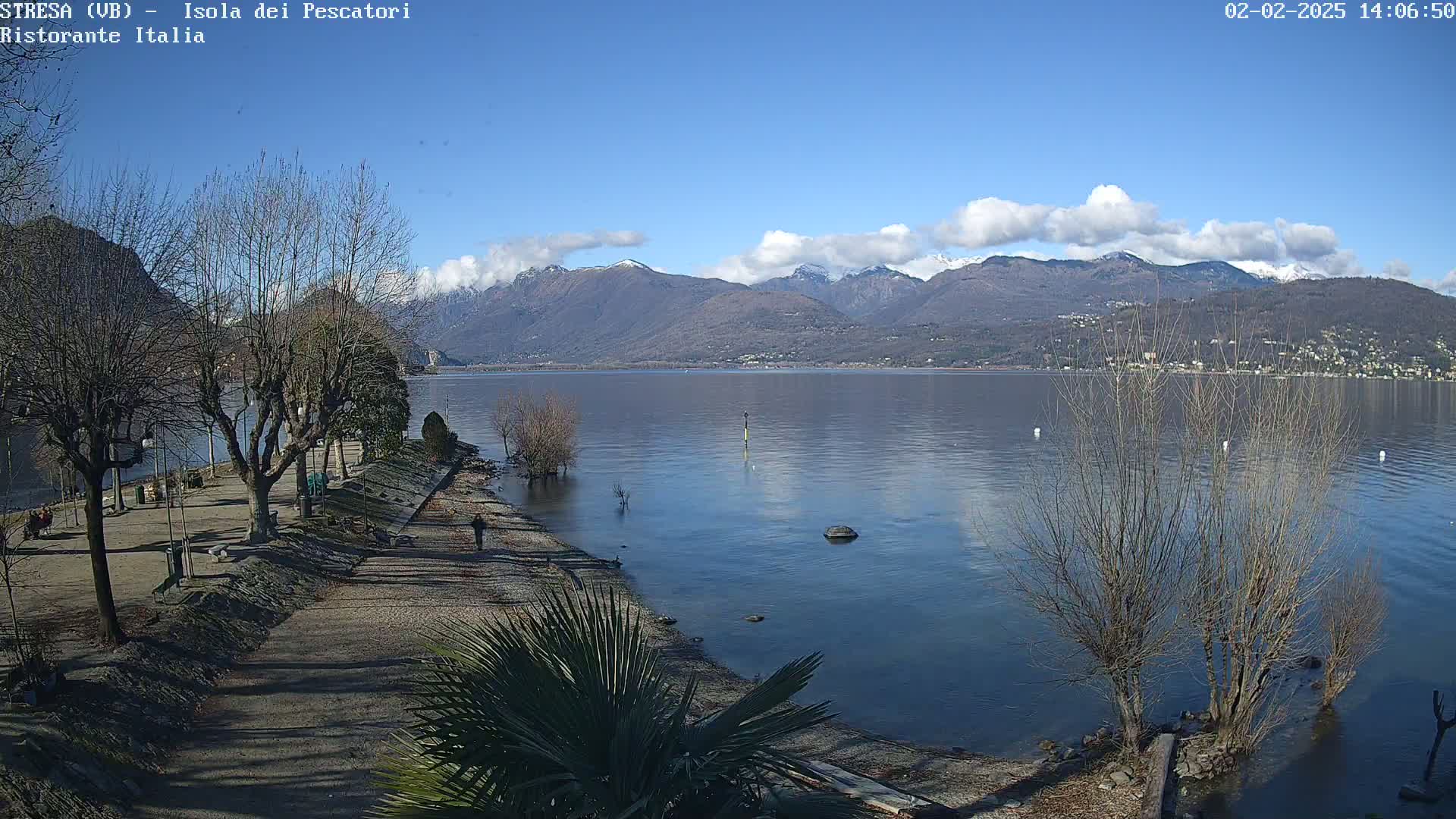 A calm lake with snow-capped mountains in the background under a mostly clear blue sky.