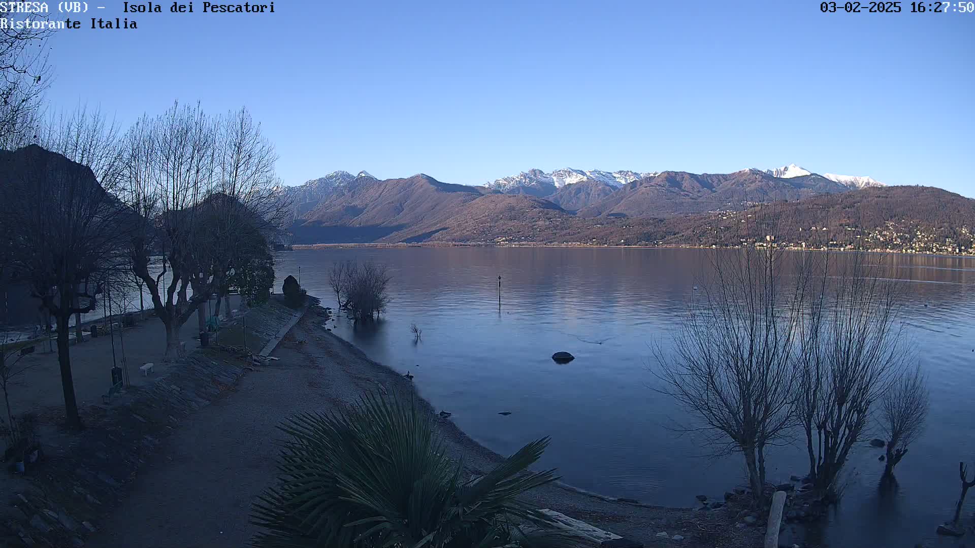 A calm lake with snow-capped mountains in the background under a clear blue sky.