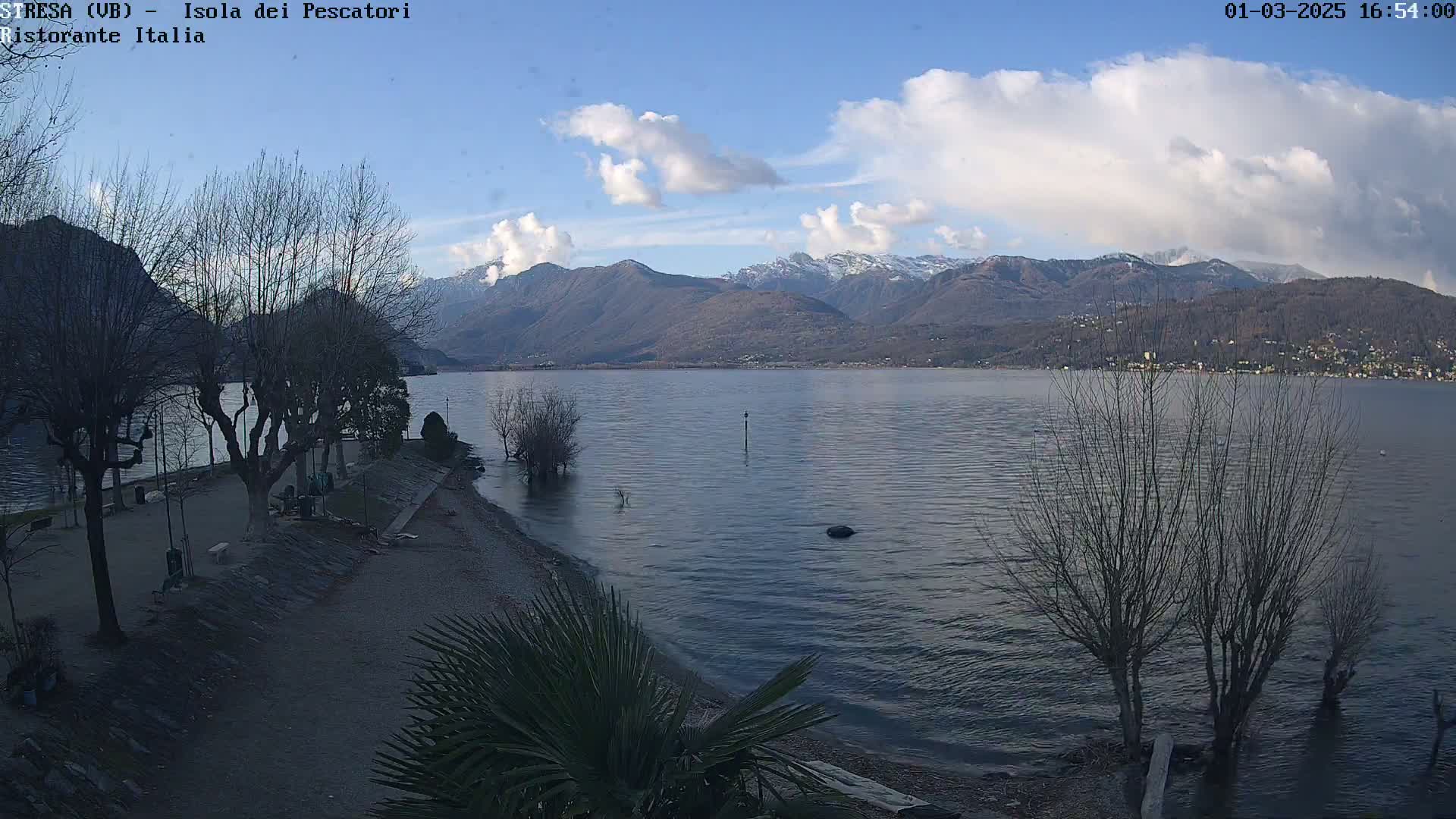 A calm lake with snow-capped mountains in the background under a partly cloudy sky.