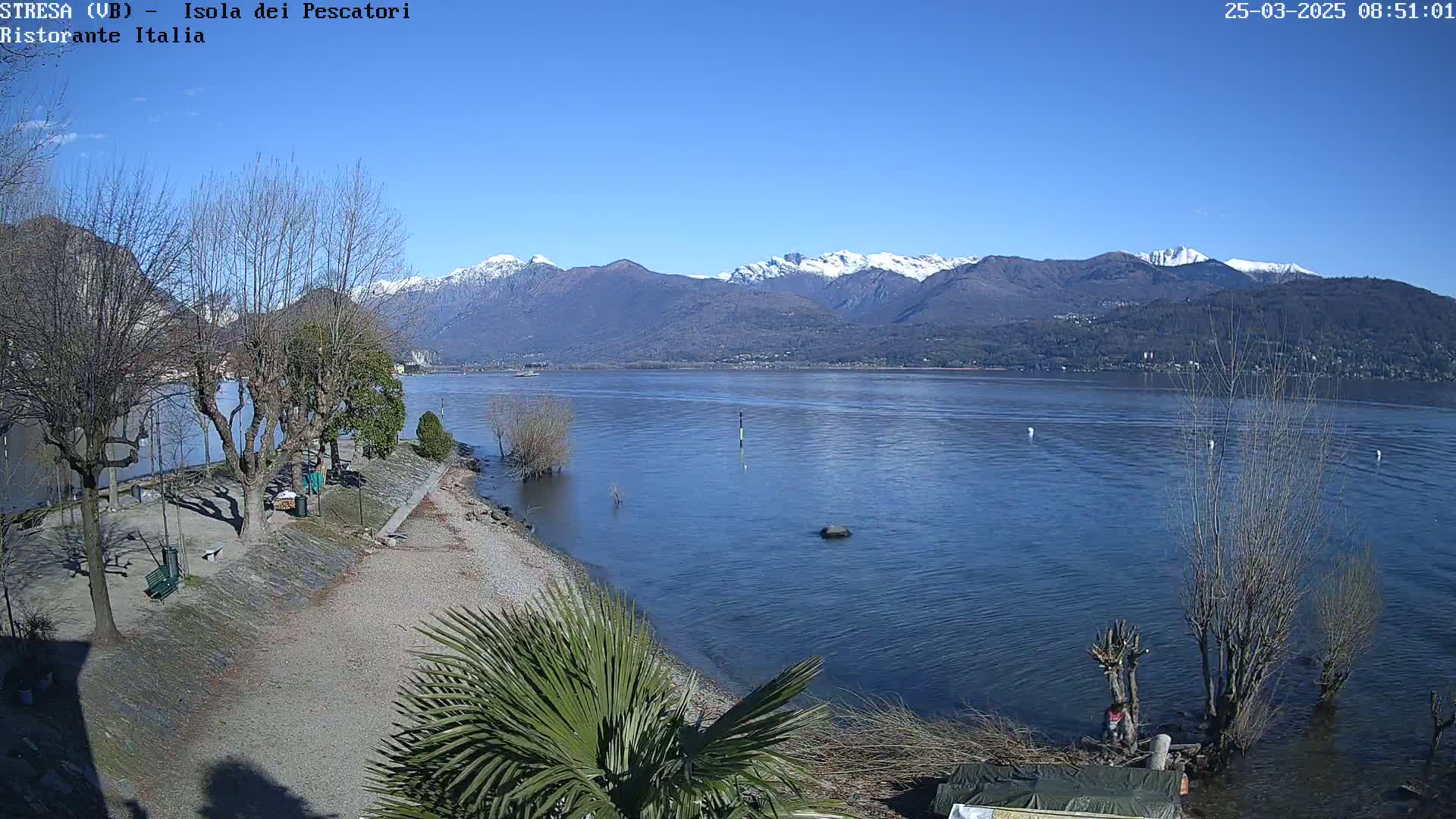A calm lake with snow-capped mountains in the background on a sunny day.