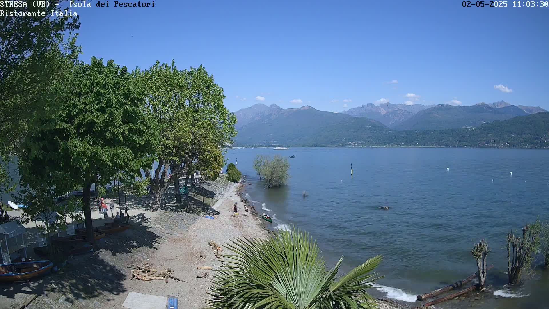 A sunny day at a lakeside beach with people enjoying the shore, under a clear blue sky and mountains in the distance.