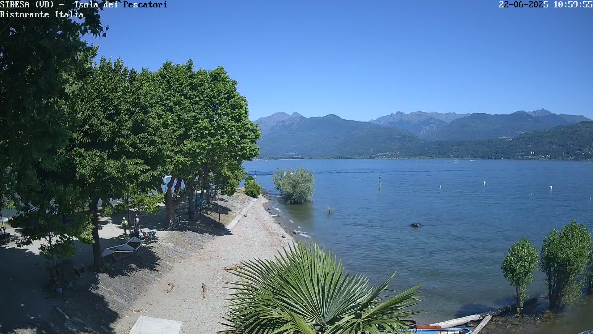 A sunny day shows a sandy beach with trees and a calm lake, mountains in the background.