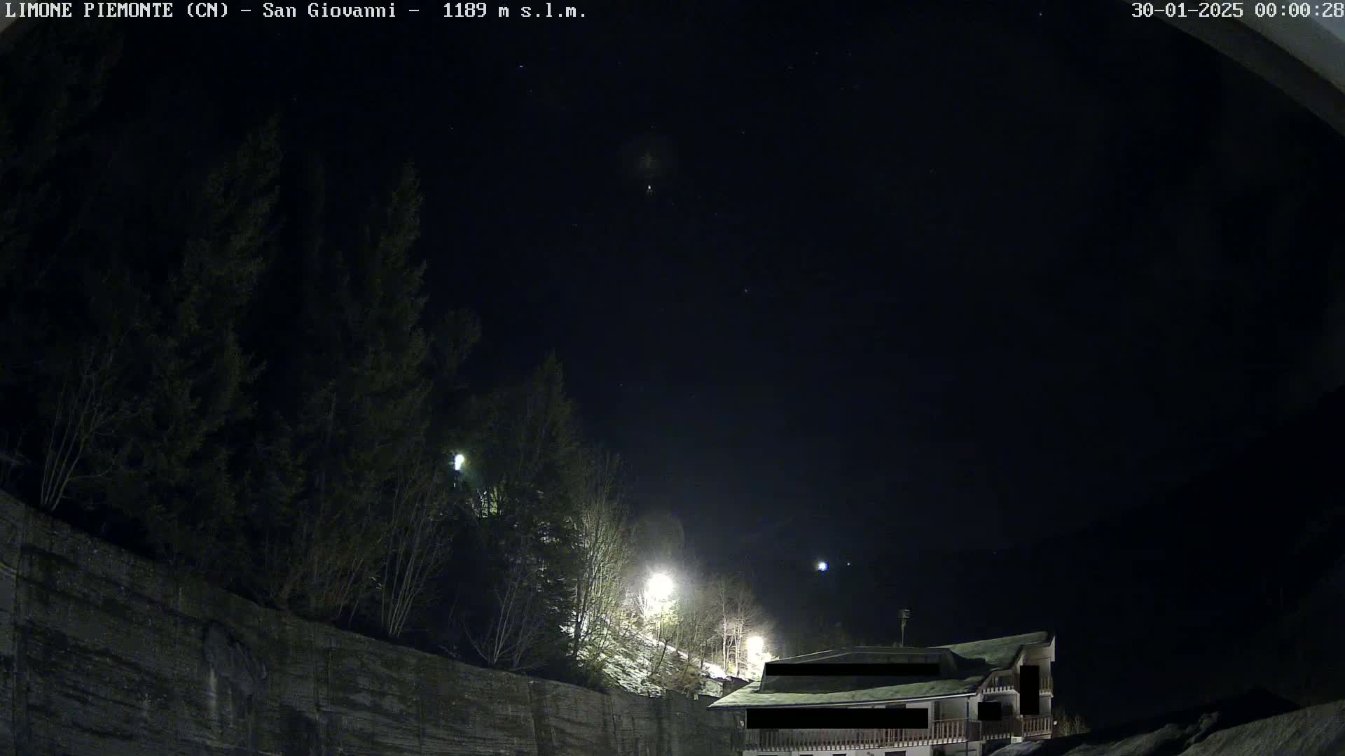 A nighttime view of a building partially obscured by darkness, situated on a hillside amongst evergreens under a clear, starry sky with a dusting of snow visible on the ground.