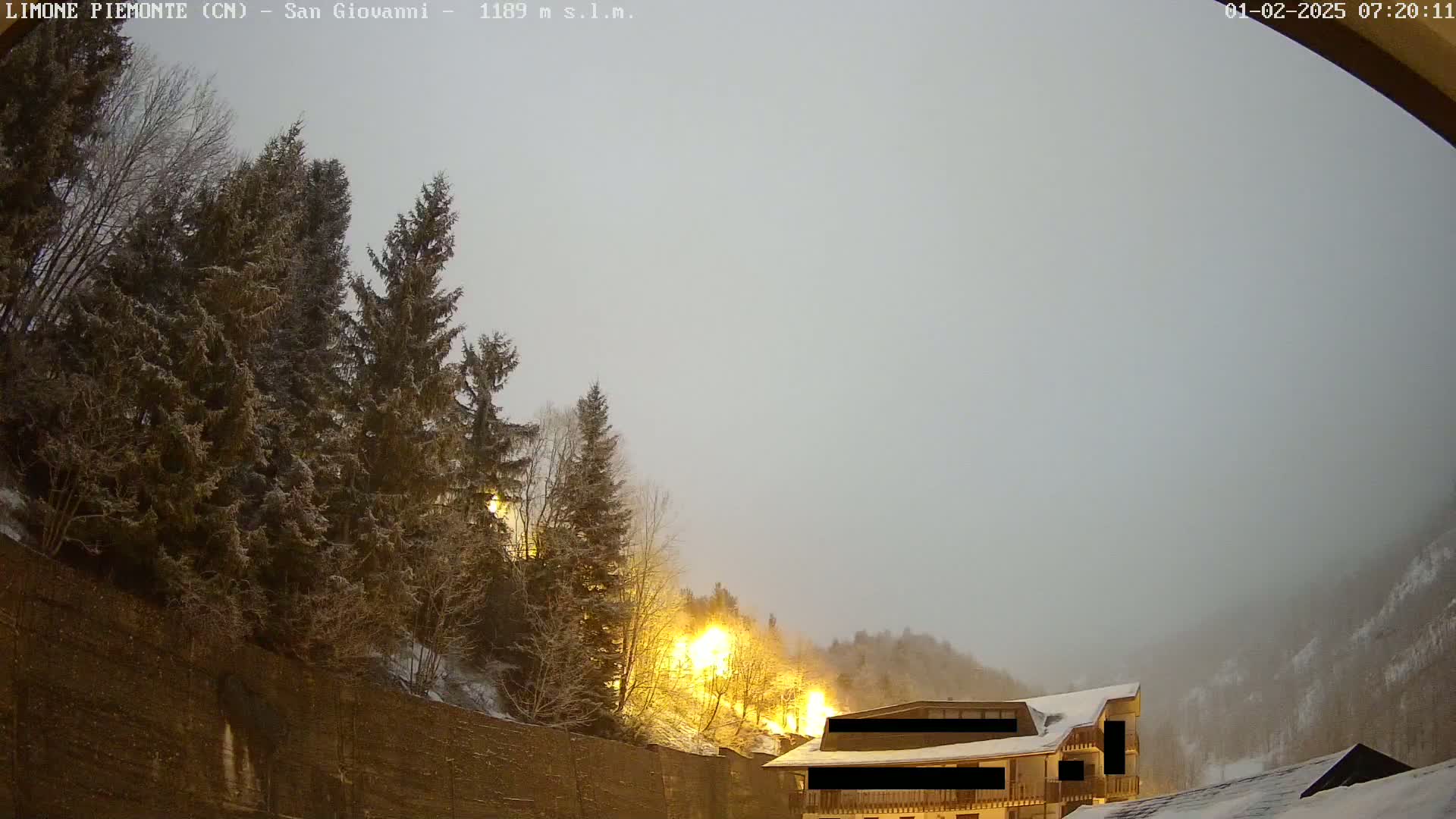 A snow-covered hillside with evergreens and a building is visible under an overcast sky.