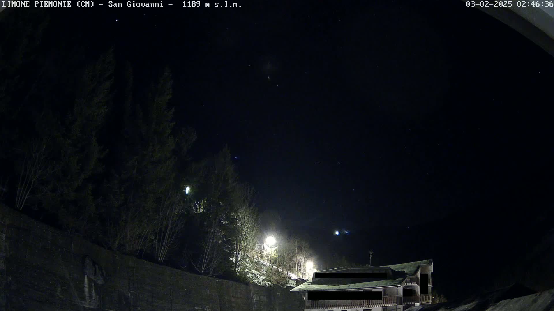 A night scene shows a building partially visible under a dark, starlit sky, with trees and a low wall in the foreground, and some snow on the ground.