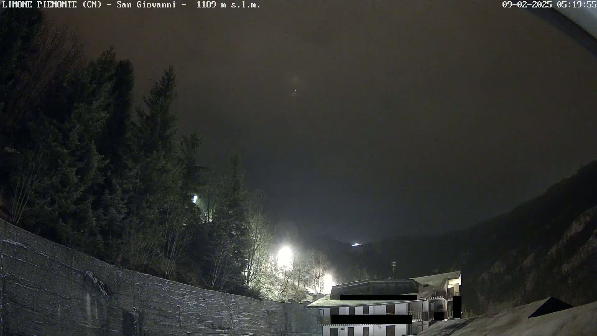 A nighttime view of a building nestled among dark, snow-covered trees under a hazy, dark sky.